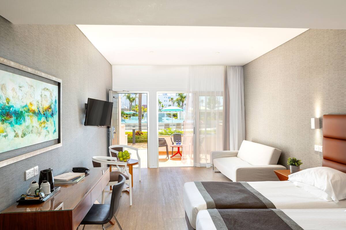Una habitación de hotel moderna con escritorio, cama, sofá y un gran ventanal con vistas al exterior.
