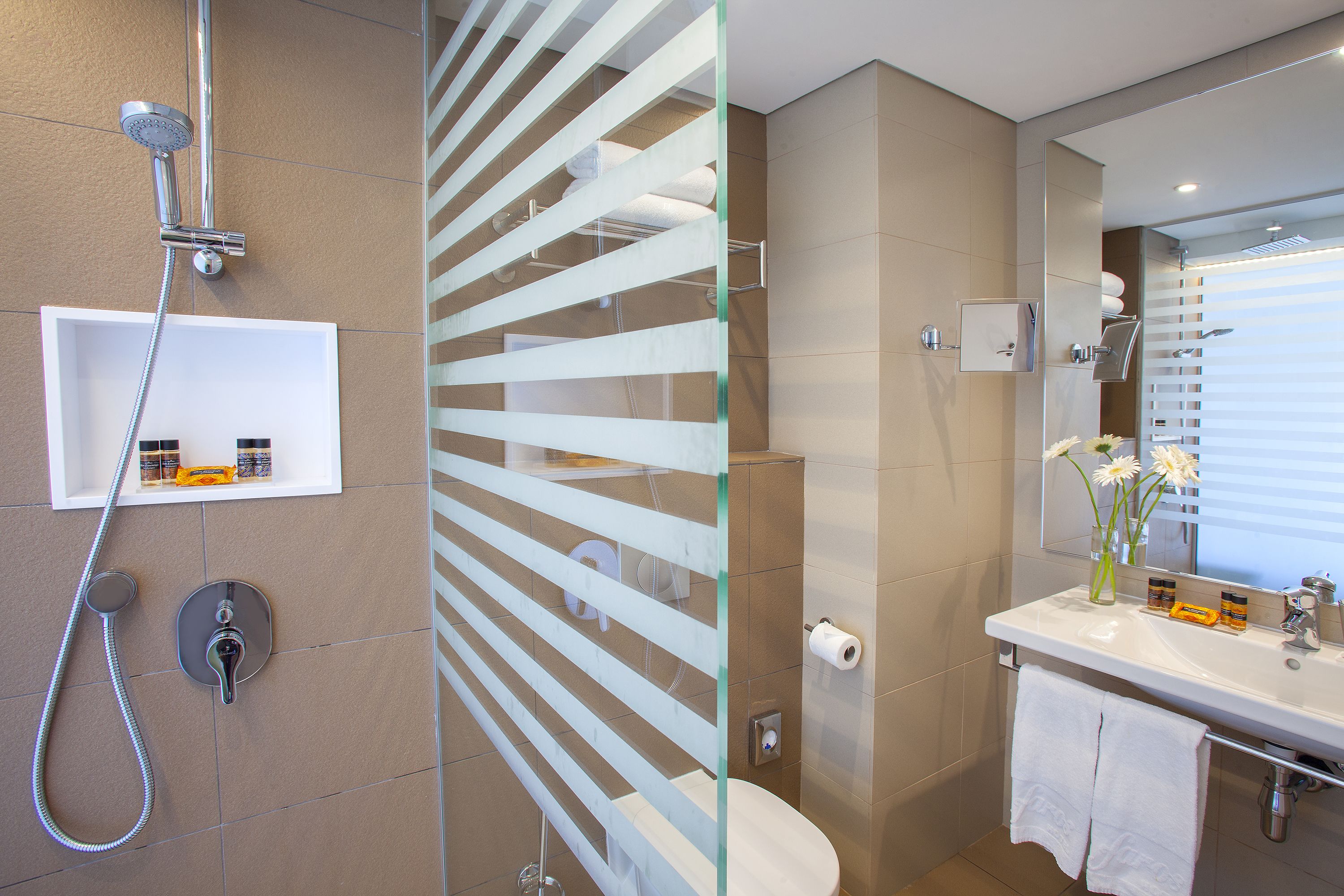 A modern bathroom with a glass partition, a shower, a toilet, and a sink with toiletries.