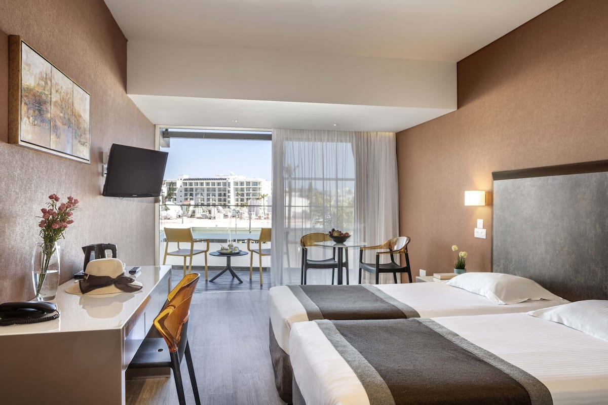 Habitación de hotel con dos camas, un escritorio, una silla, un televisor y vista a la ciudad.