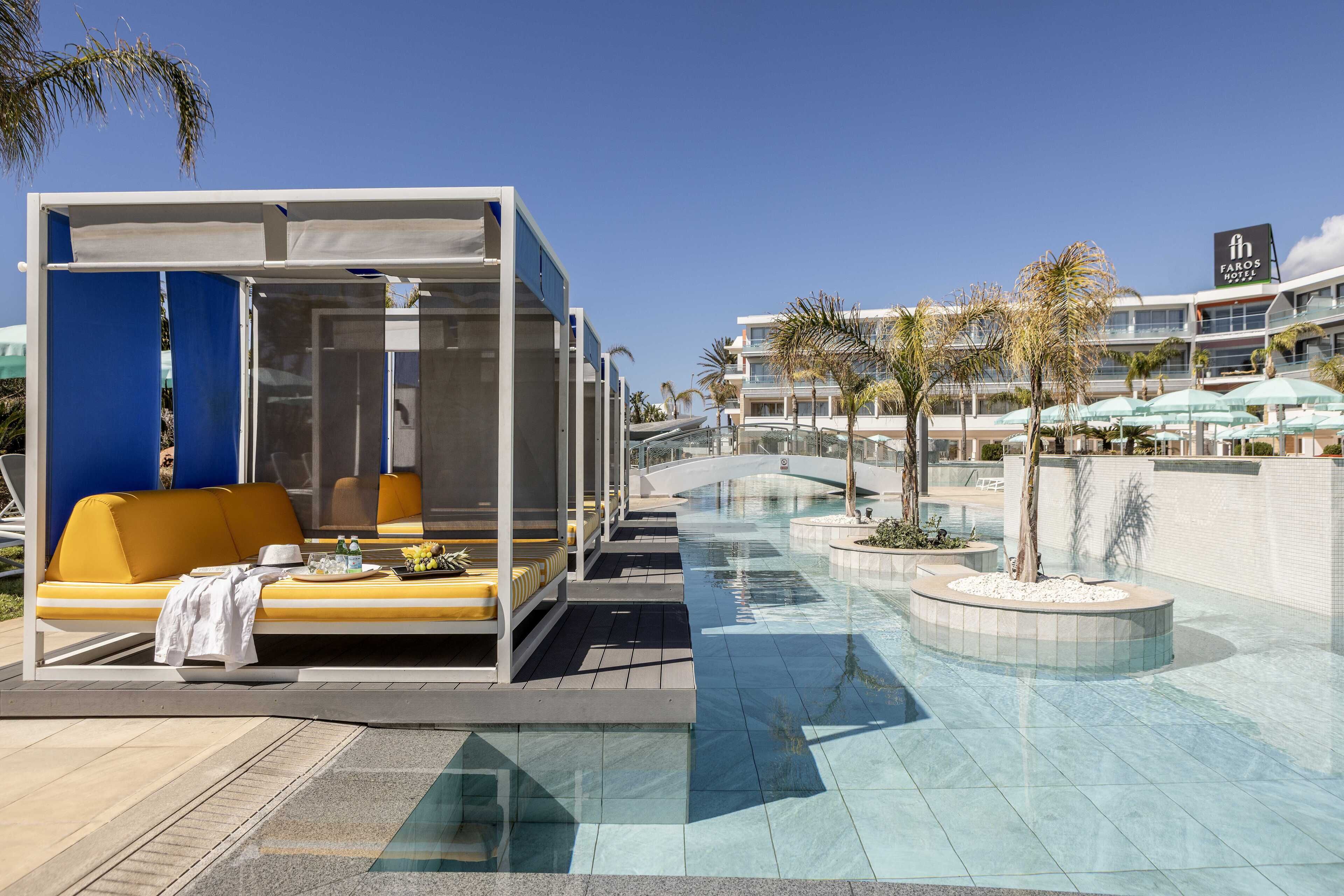 A modern hotel lobby with a pool, outdoor seating, and a view of the hotel buildings.