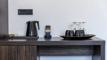 Una habitación de hotel moderna con un escritorio de madera, una cafetera, un teléfono inteligente y una bandeja con vasos y una botella.