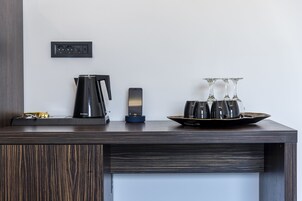 Una habitación de hotel moderna con un escritorio de madera, una cafetera, un teléfono inteligente y una bandeja con vasos y una botella.