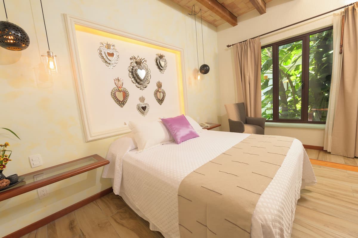 Un dormitorio con una cama grande, una mesita de noche, una silla, un ventanal con cortinas y espejos con forma de corazón en la pared.