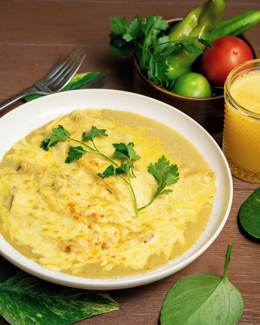 A bowl of creamy soup garnished with parsley, accompanied by a glass of orange juice and a bowl of fresh vegetables.
