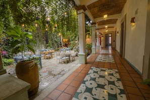 Un patio interior con suelo de baldosas, mesas, sillas y plantas en macetas.