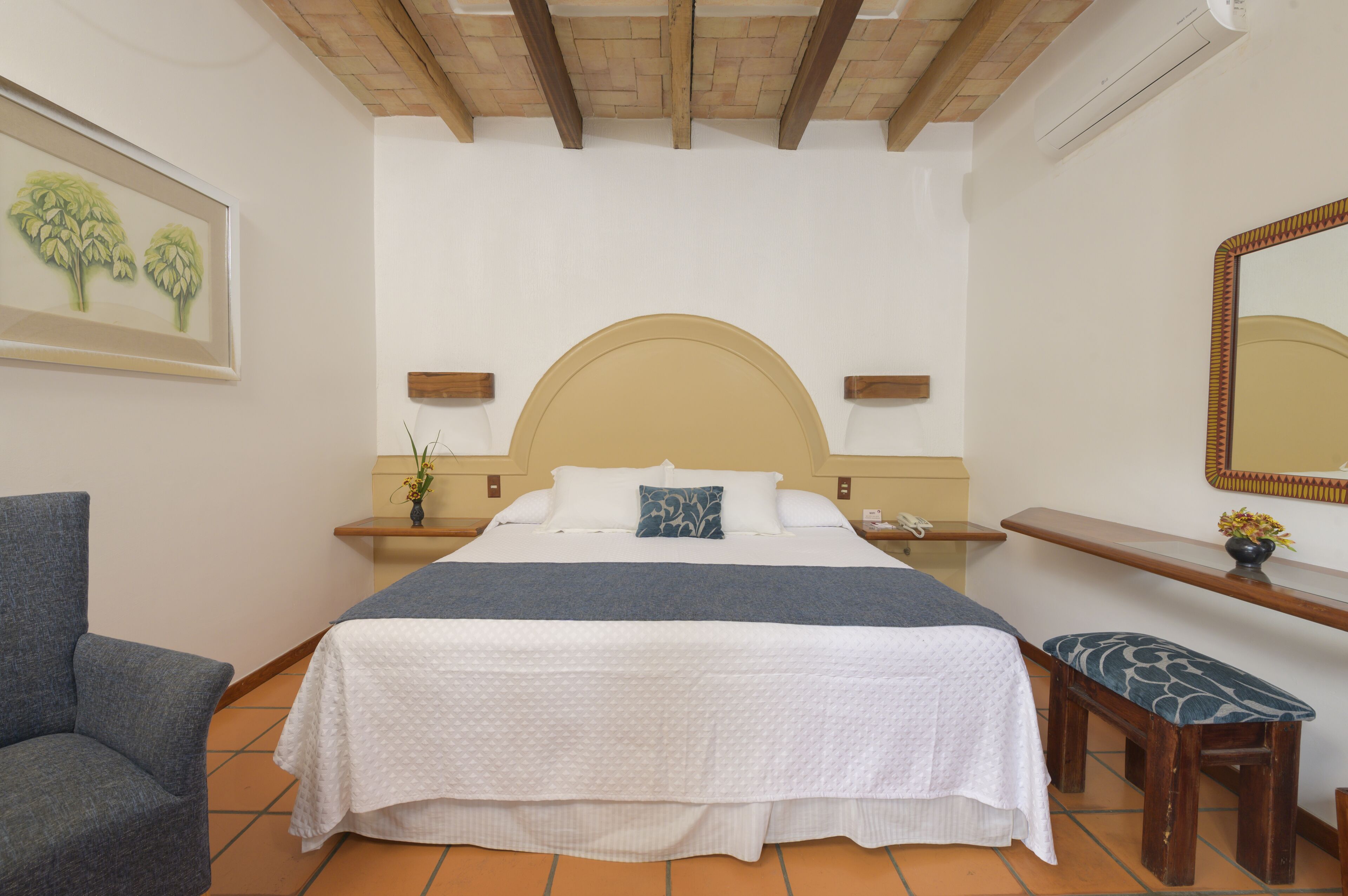Un dormitorio con una cama grande, una silla, un banco, una mesita de noche, un espejo y un estante en la pared.