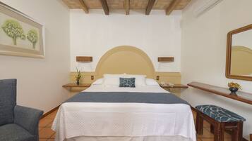 Un dormitorio con una cama grande, una silla, un banco, una mesita de noche, un espejo y un estante en la pared.