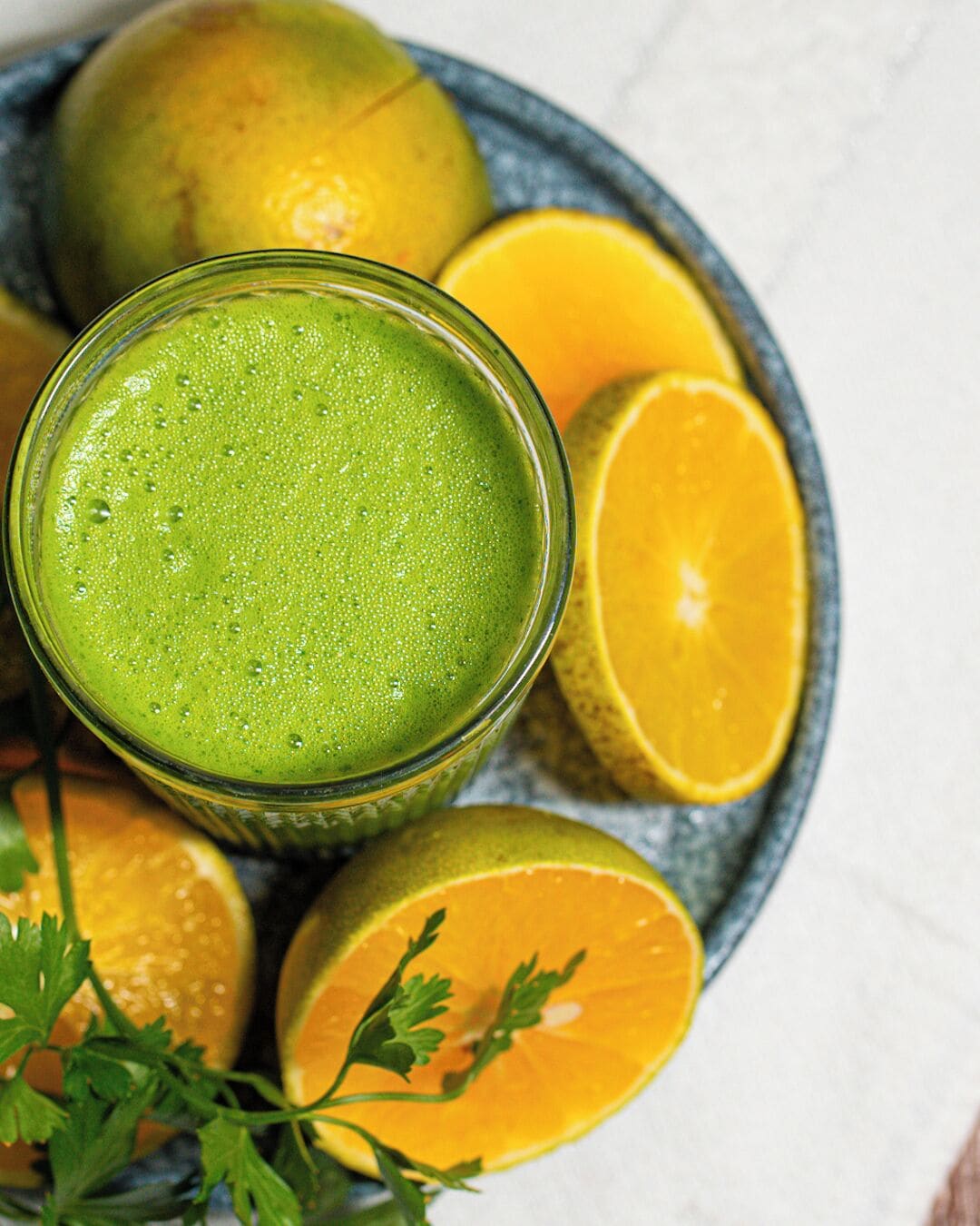 A glass of green smoothie with lime and orange slices on a plate.