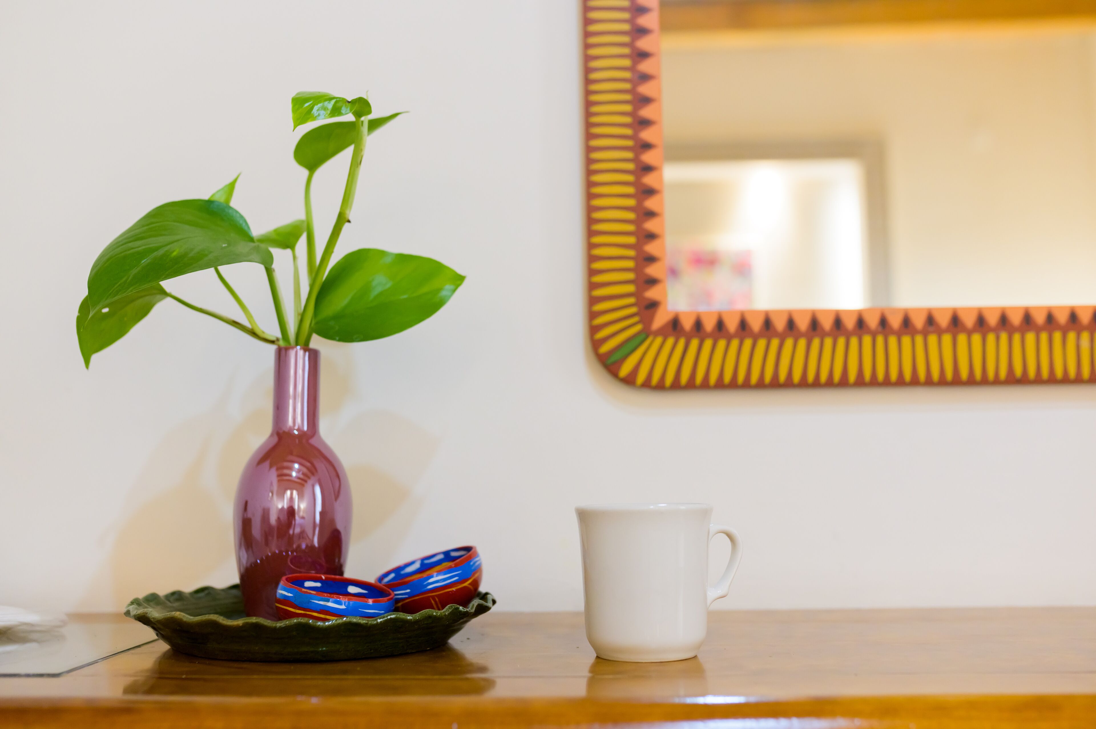 A potted plant in a vase, a white mug, and a decorative mirror on a wooden surface.
