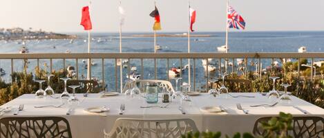 Un área de comedor al aire libre con vistas al mar, banderas y una mesa lista para una comida.