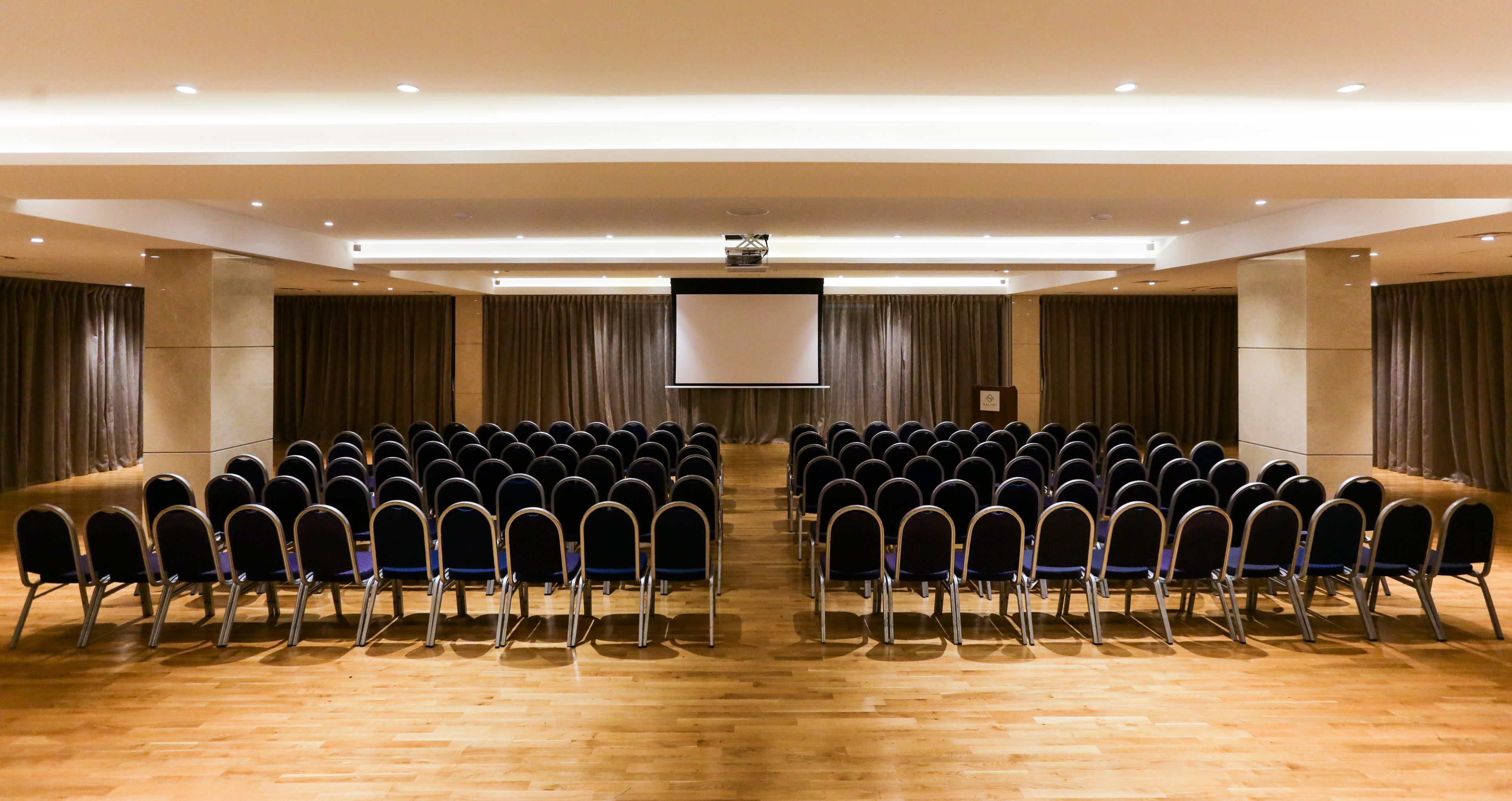 A conference room with rows of chairs, a large screen, and a podium.