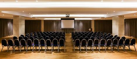 A conference room with rows of chairs, a large screen, and a podium.