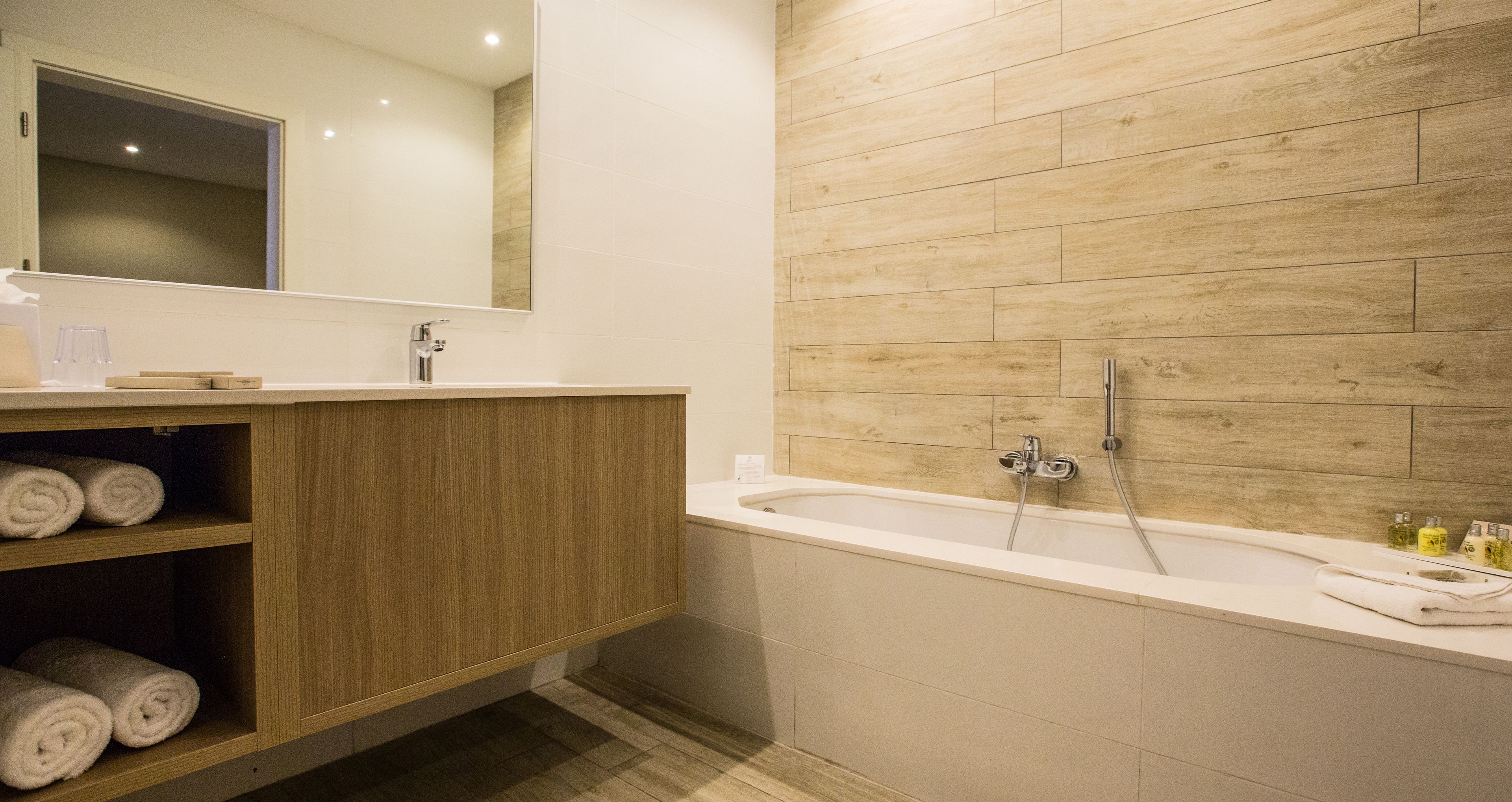 Ein modernes Badezimmer mit einem Holzwaschtisch, einem großen Spiegel und einer Badewanne.