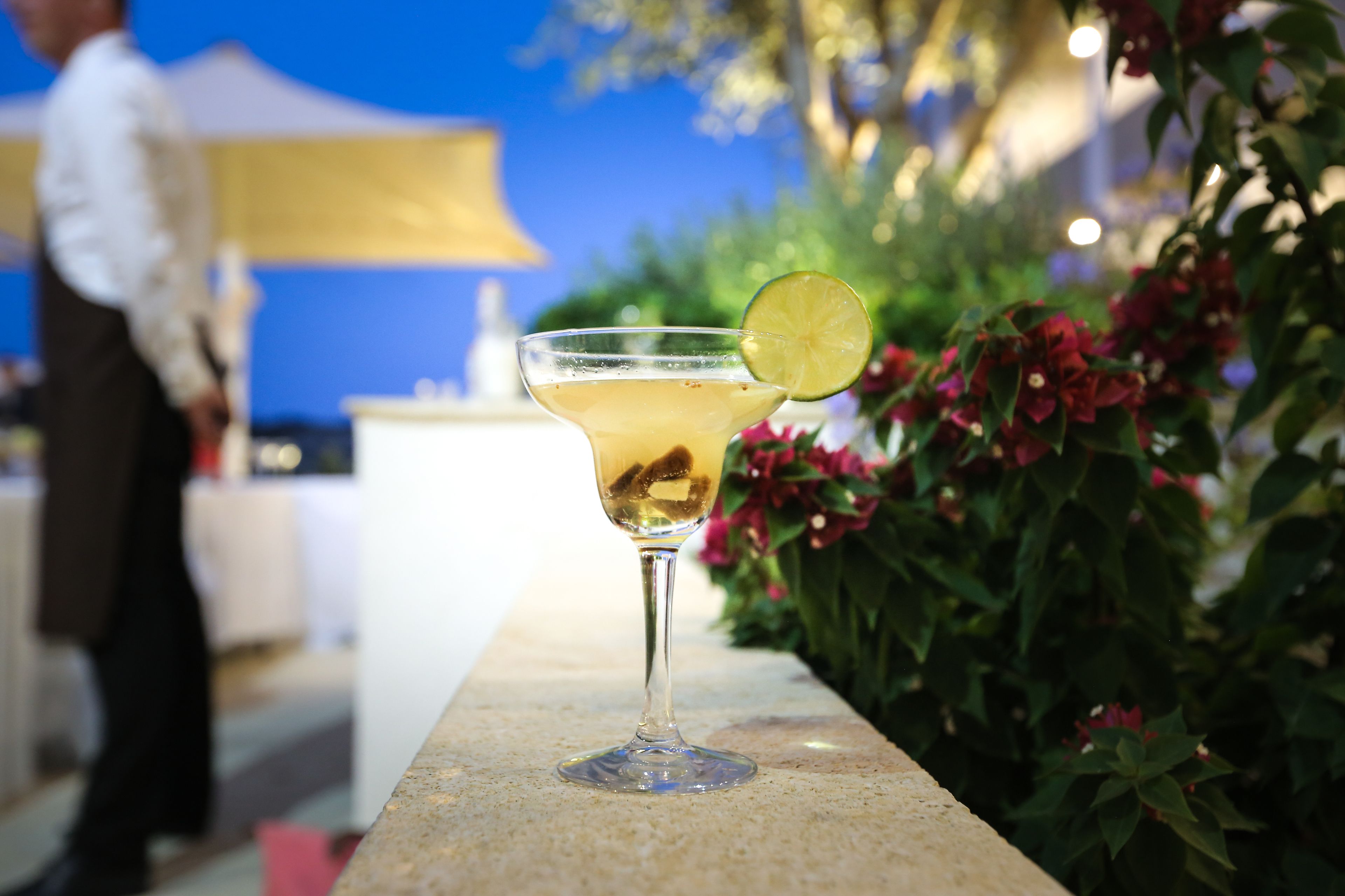 Un verre à cocktail, garni d’une tranche de citron vert, posé sur un comptoir en pierre.