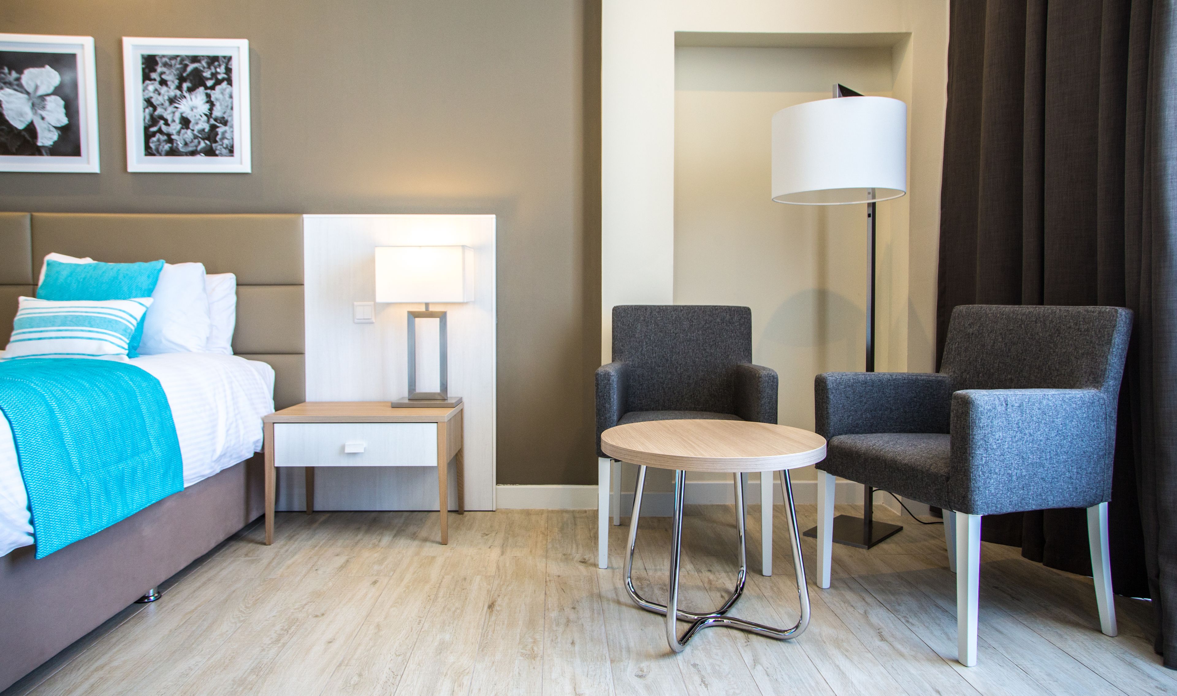 Une chambre d’hôtel comprenant un lit, une table de chevet, une lampe, deux fauteuils et une petite table ronde.