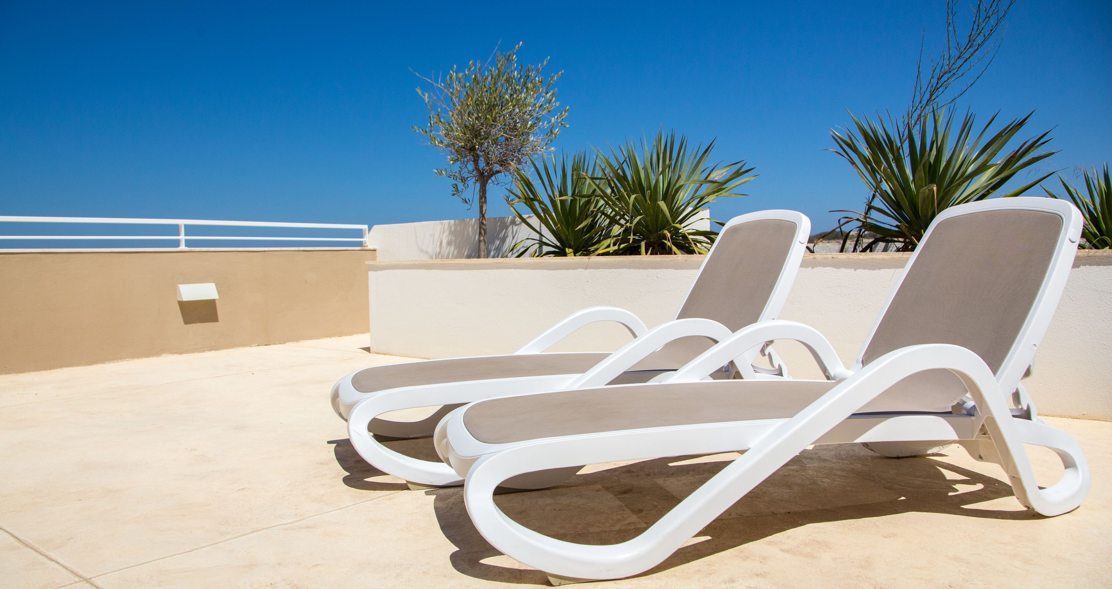 Deux fauteuils de jardin blancs avec des coussins beige, sur une terrasse carrelée.