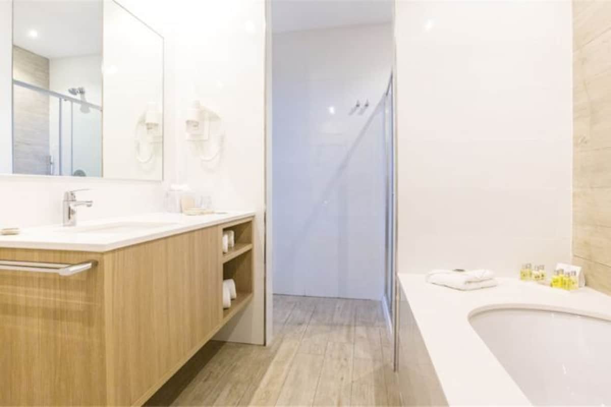 A modern bathroom with a wooden vanity, a large mirror, a shower area, and a bathtub.