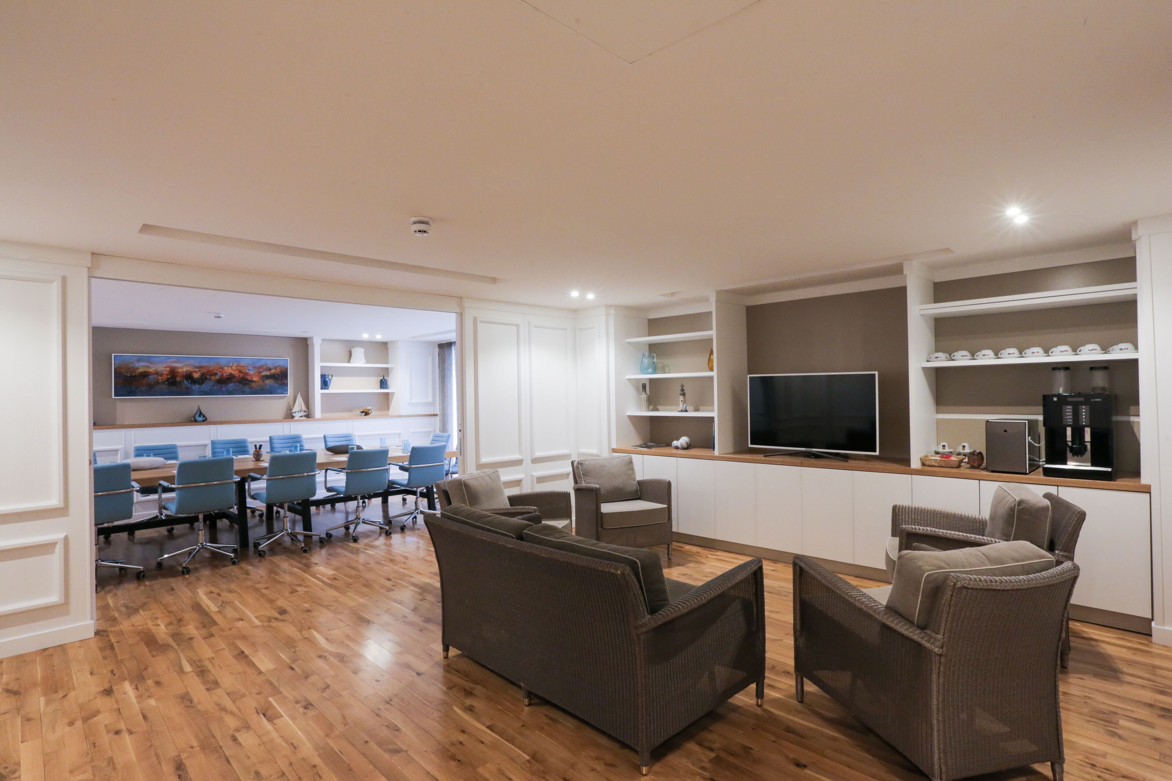 A modern living room with a wooden floor, a large flat-screen TV, and a dining area with blue chairs.