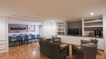 A modern living room with a wooden floor, a large flat-screen TV, and a dining area with blue chairs.