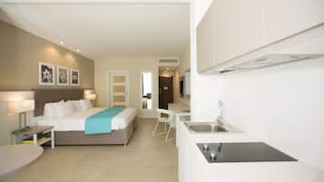 Una habitación de hotel moderna con cama, mesita de noche, lámpara y una kitchenette con fregadero y estufa.