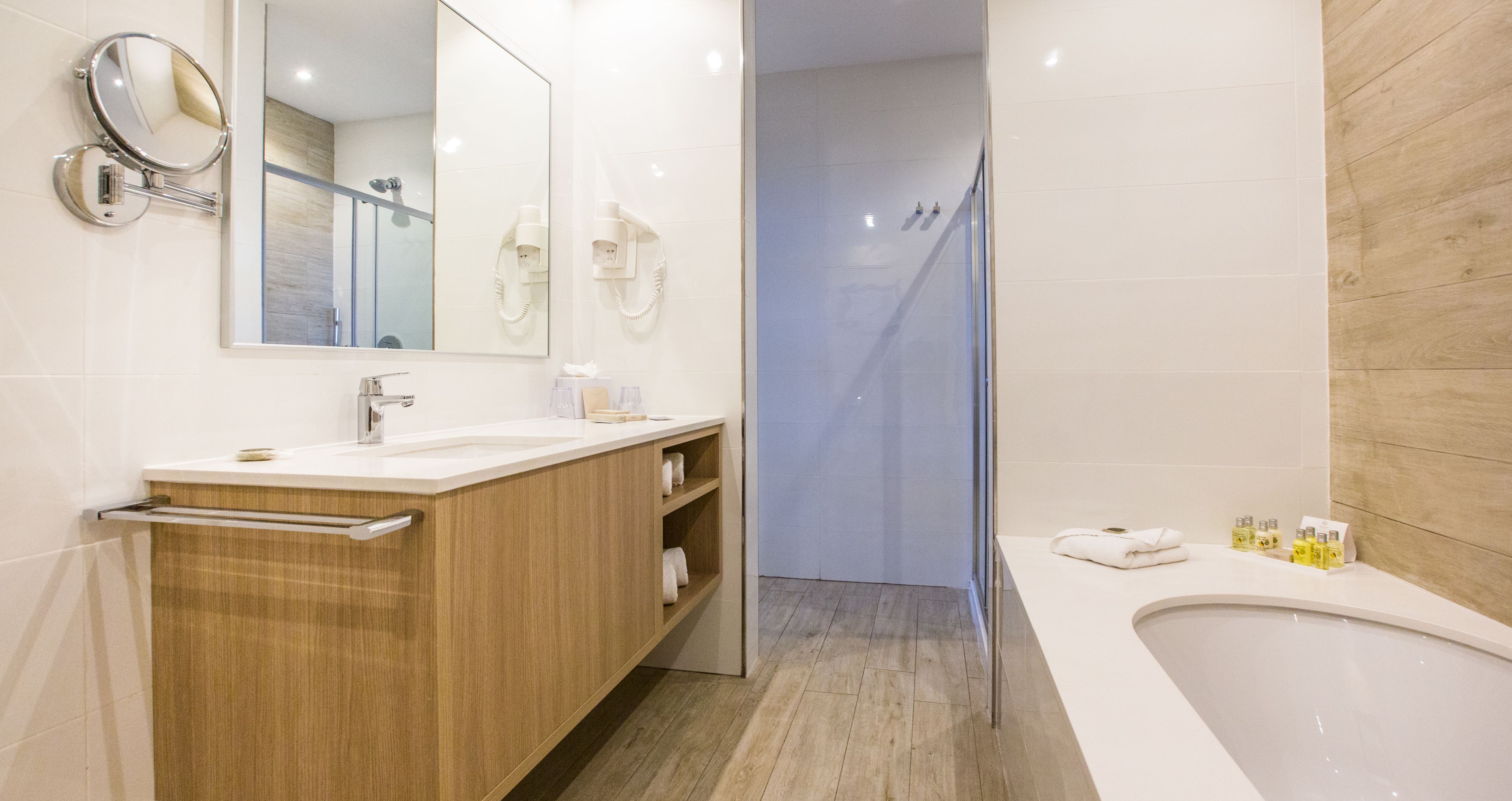 A modern bathroom with a wooden vanity, a large mirror, a bathtub, and a shower area.