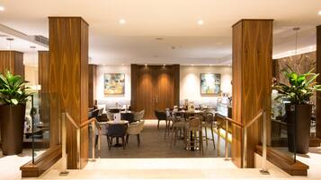 A modern hotel lobby with wooden paneling, a central seating area, and large potted plants.