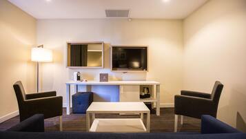 A hotel room with a TV, a desk, a coffee machine, and two armchairs.