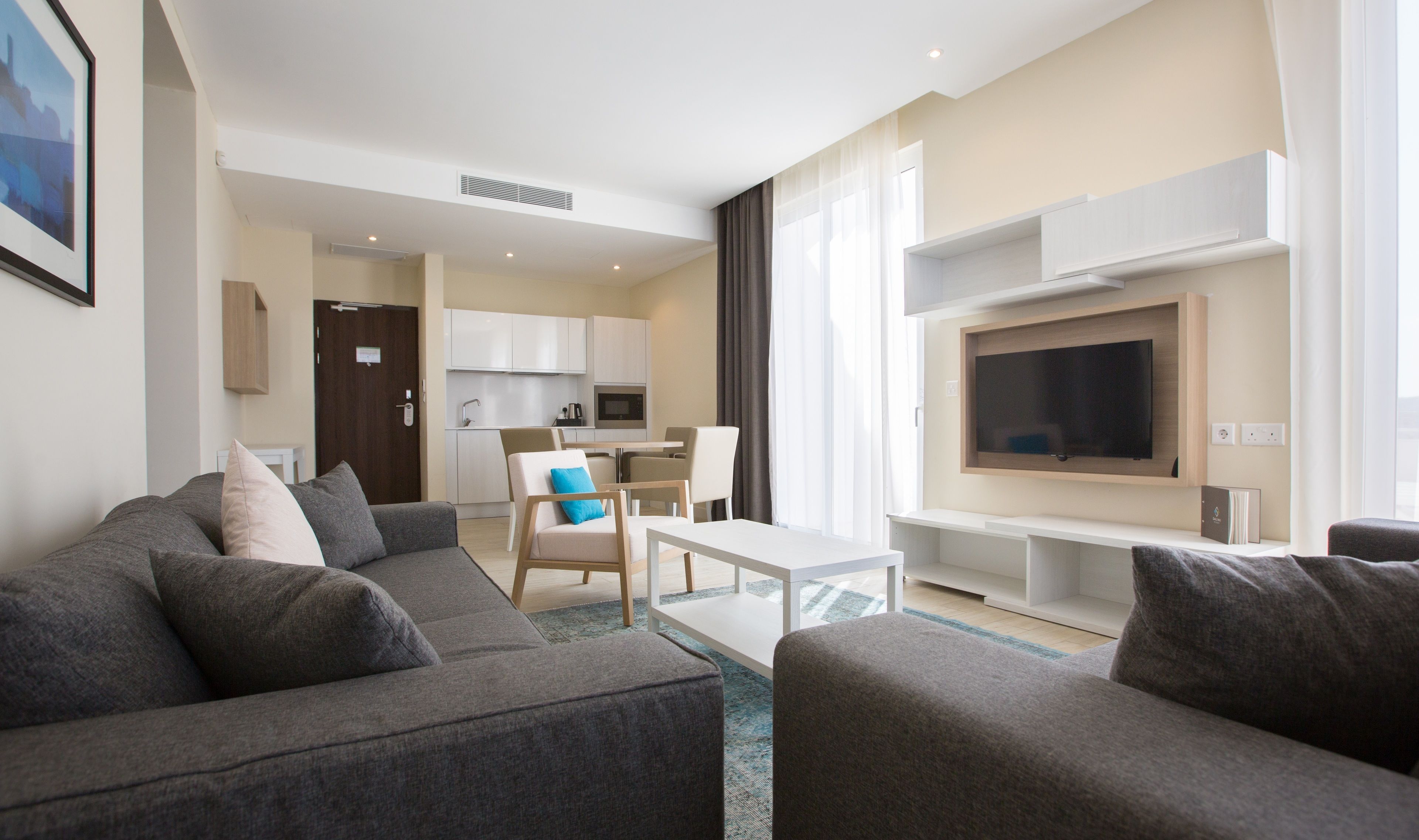 Una habitación de hotel moderna con sala de estar, kitchenette y televisor montado en la pared.