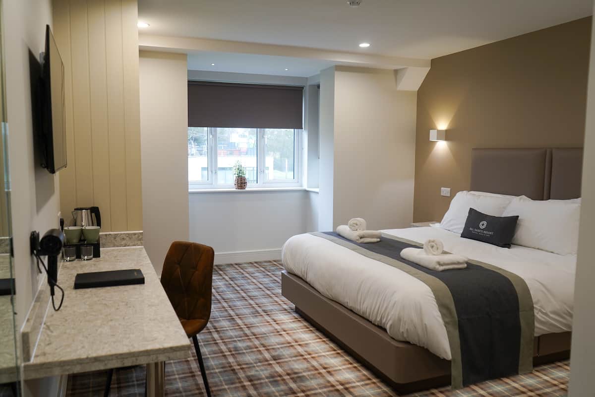 Une chambre d’hôtel avec un lit, un bureau, une chaise, une fenêtre donnant sur un beau paysage et une petite plante.