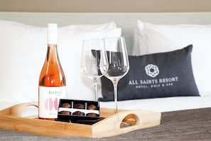 Une bouteille de vin rosé, deux verres à vin et une boîte de chocolats, le tout posé sur un plateau en bois.