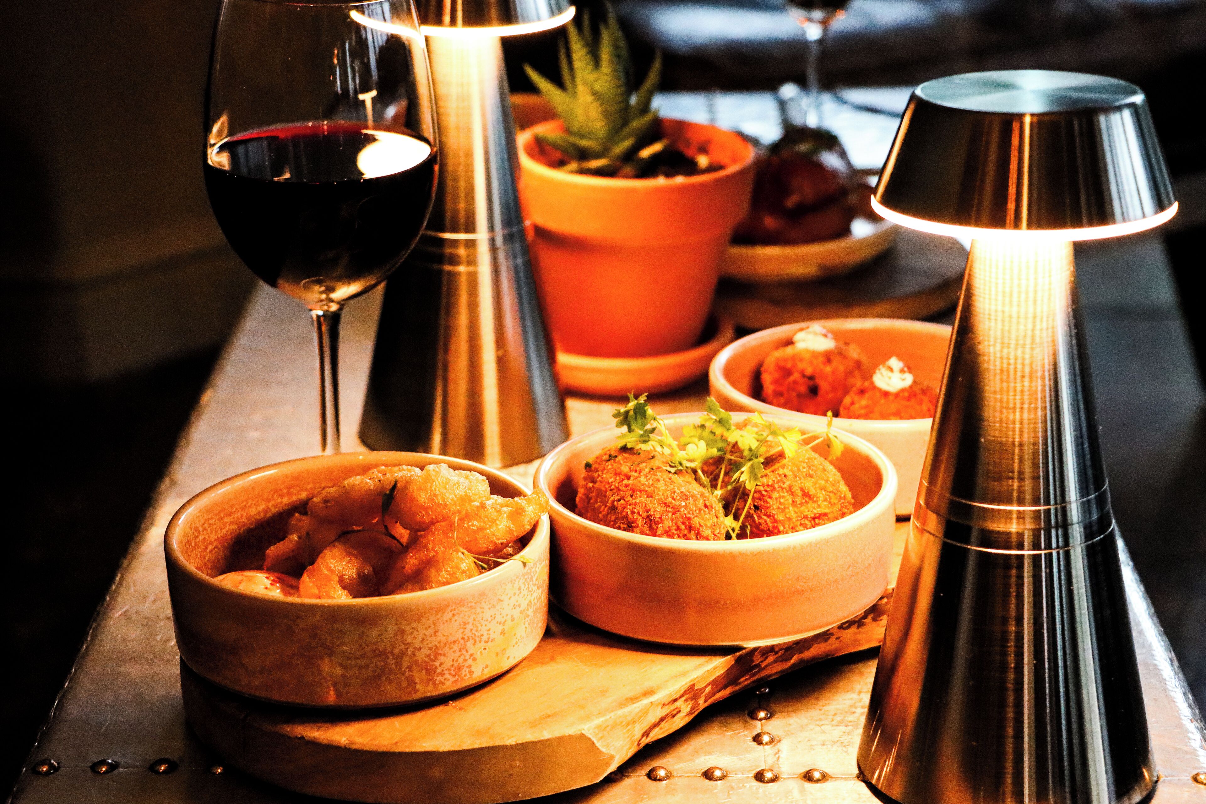 A table with various dishes, a glass of red wine, and a lit lamp.