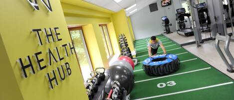 Ein Fitnessstudio mit grüner Rasenfläche, Trainingsgeräten und einem Wandschild mit der Aufschrift 'THE HEALTH HUB'.