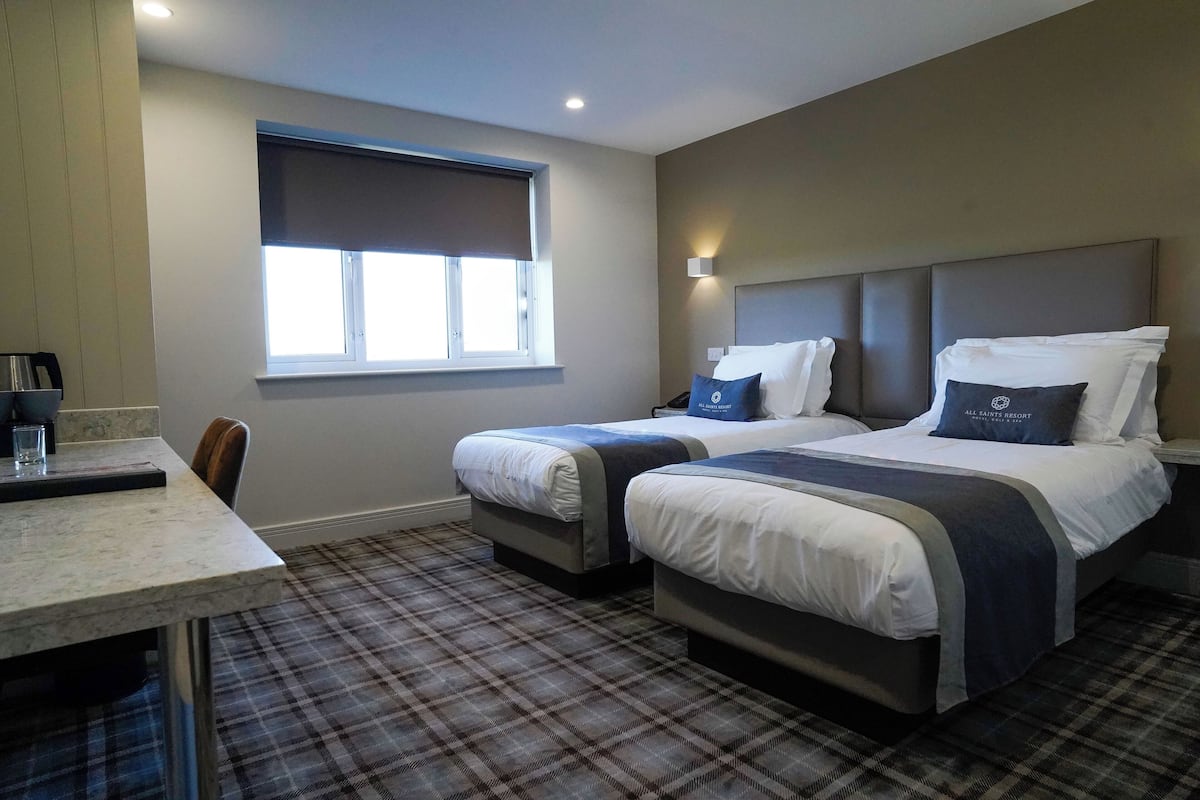 Une chambre d’hôtel avec deux lits, une table à manger, une fenêtre avec des stores et un tapis à carreaux.