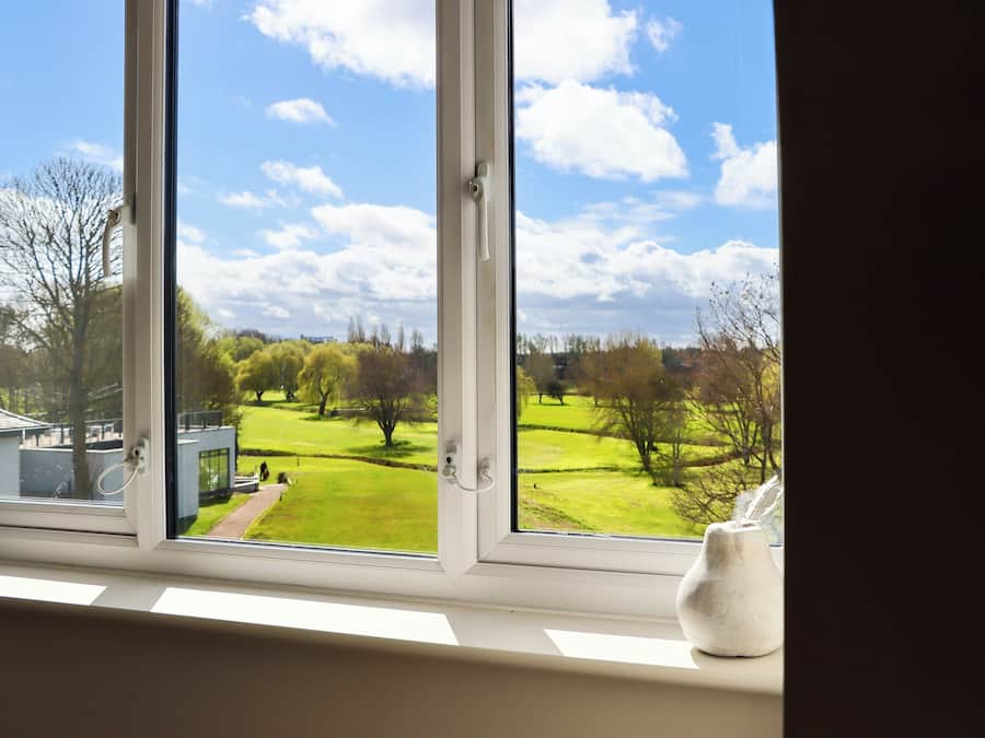 A window with a view of a green landscape, a white vase, and a door handle.