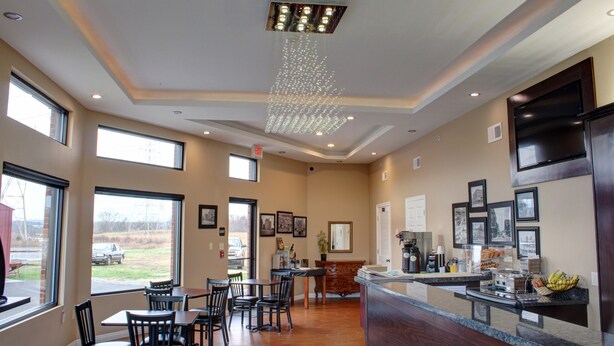 A hotel lobby with a dining area, a reception desk, and a view of the outdoors. - Luxbury Inn & Suites (Maryville)