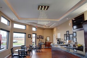 A hotel lobby with a dining area, a reception desk, and a view of the outdoors. - Luxbury Inn & Suites (Maryville)
