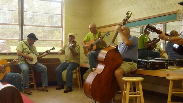 Un grupo de músicos tocando diferentes instrumentos en una habitación con ventanas grandes y un banco de madera.