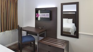 A hotel room with a bed, a desk, a chair, a dresser, a TV mounted on the wall, and a mirror. - Luxbury Inn & Suites (Maryville)