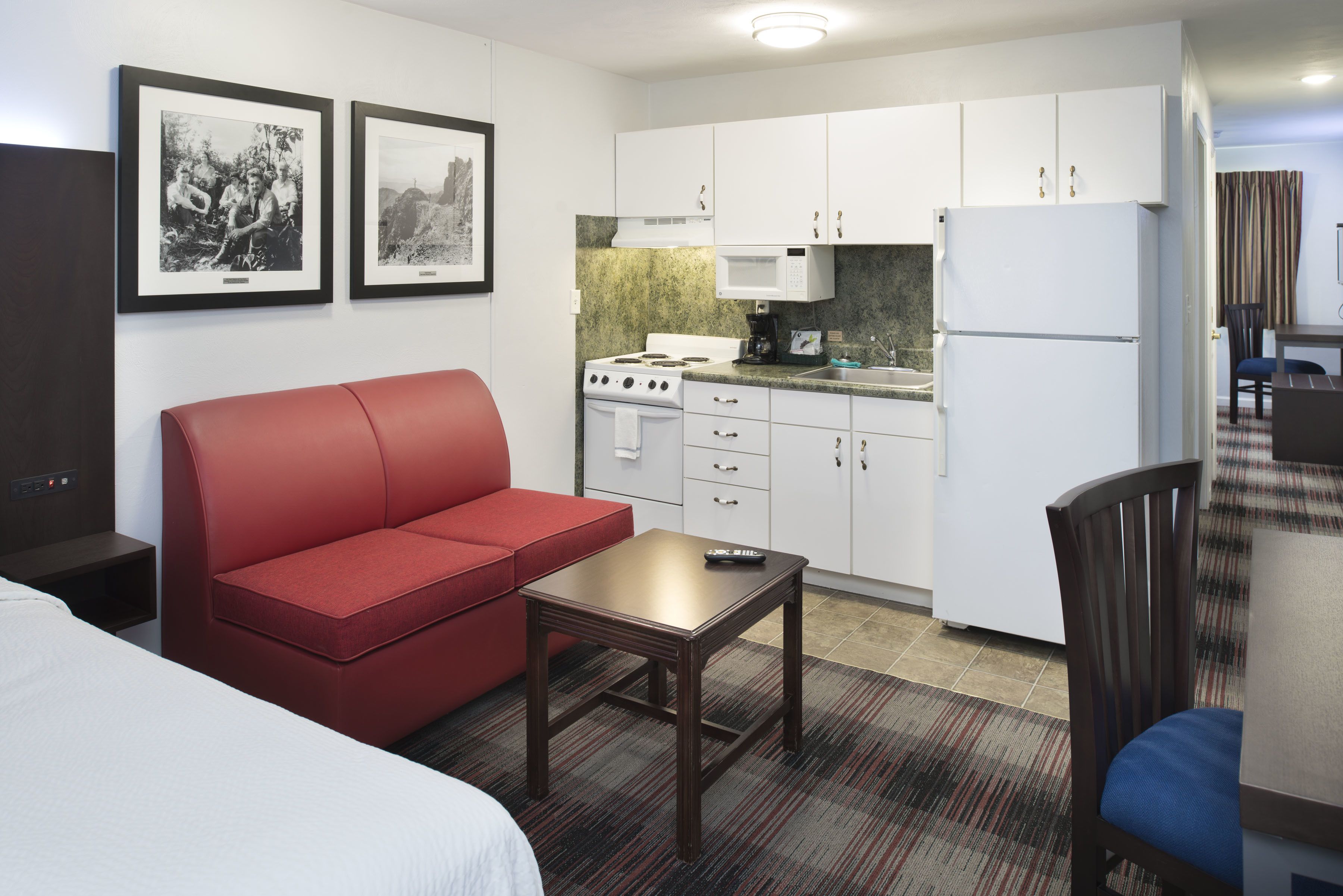 Une chambre d’hôtel compacte comprenant un coin cuisine, un canapé rouge, une petite table et un lit.