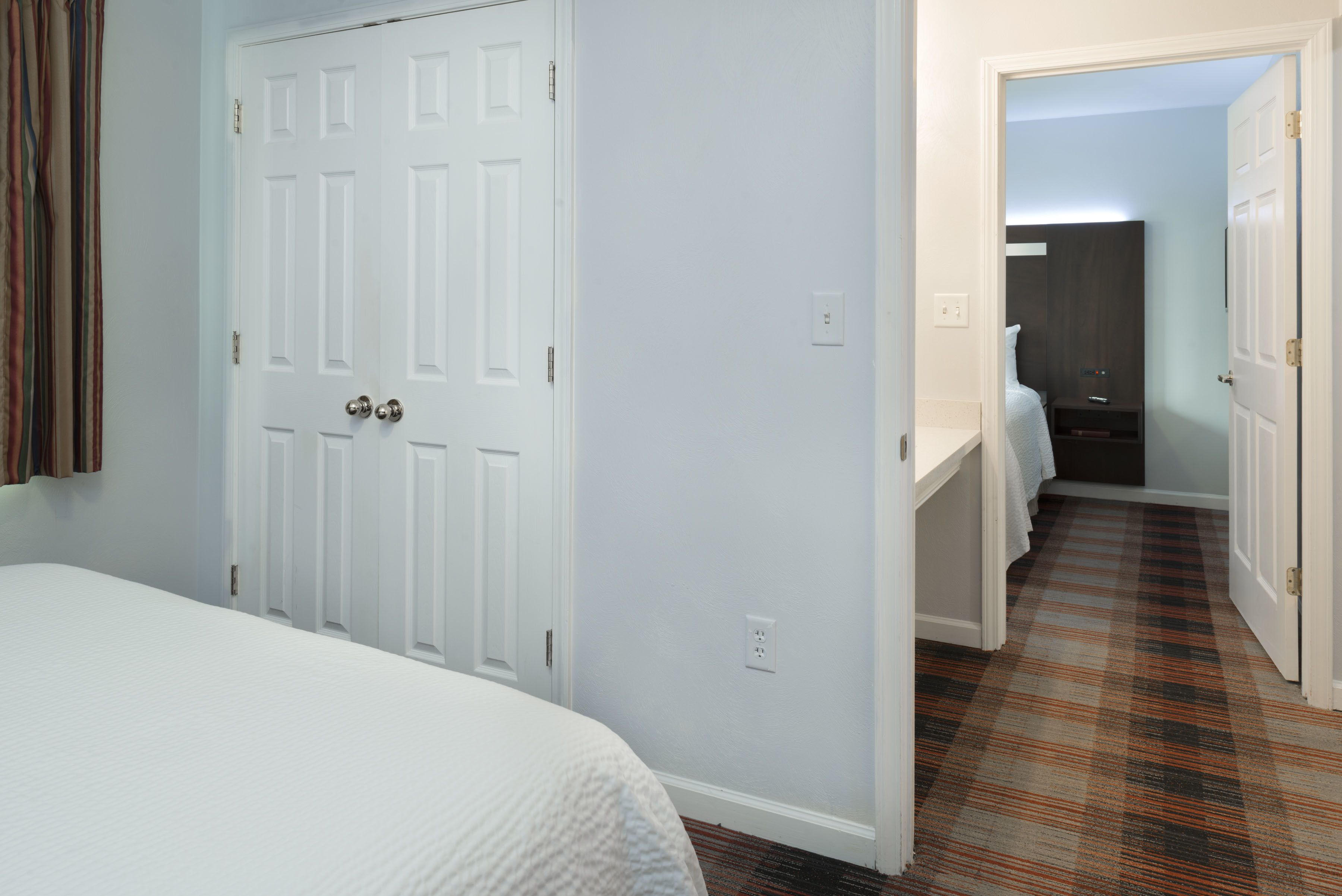 Una habitación de hotel con cama, puerta, baño y piso alfombrado.