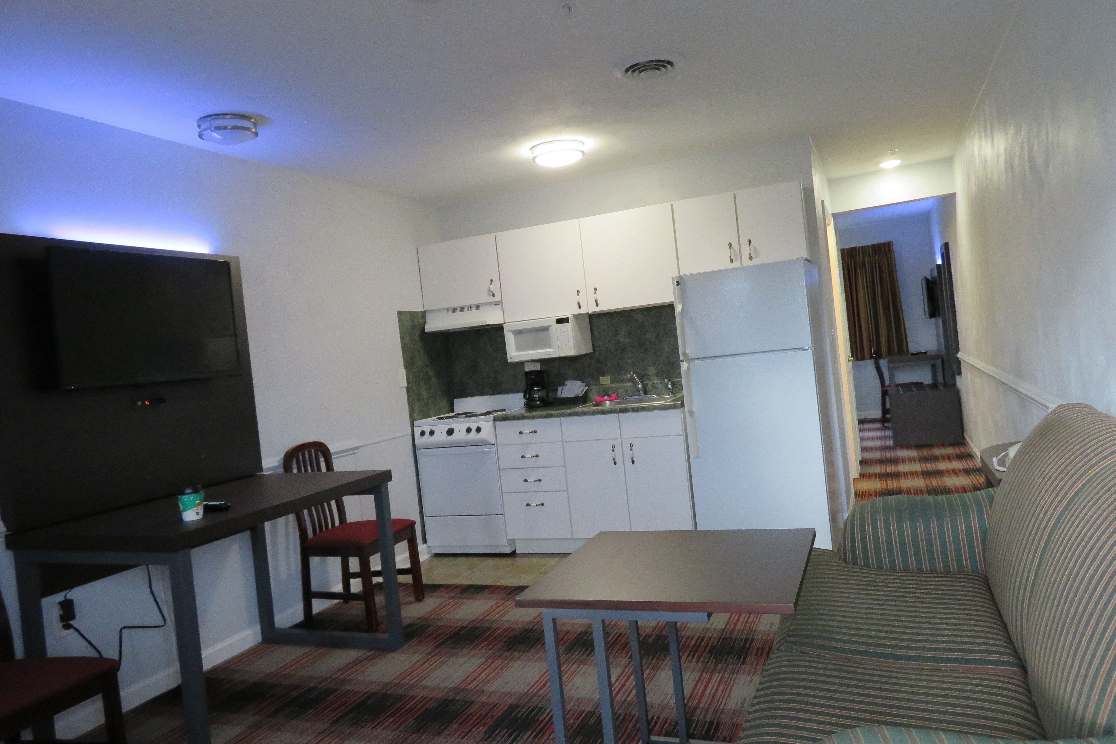A compact kitchen with white cabinets, a microwave, a stove, and a refrigerator. There is a dining table with chairs and a sofa in the living area.
