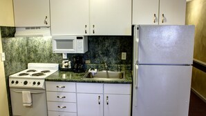 A kitchen with white cabinets, a microwave, a stove, a sink, and a refrigerator. - Luxbury Inn & Suites (Maryville)
