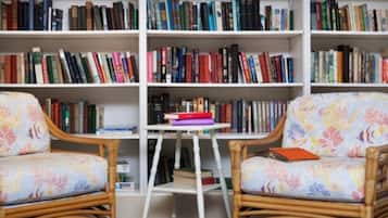 A room with two wicker chairs, a small table, and a bookshelf filled with books.