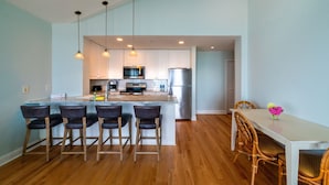 A modern kitchen with a central island, bar stools, and a dining table with chairs.