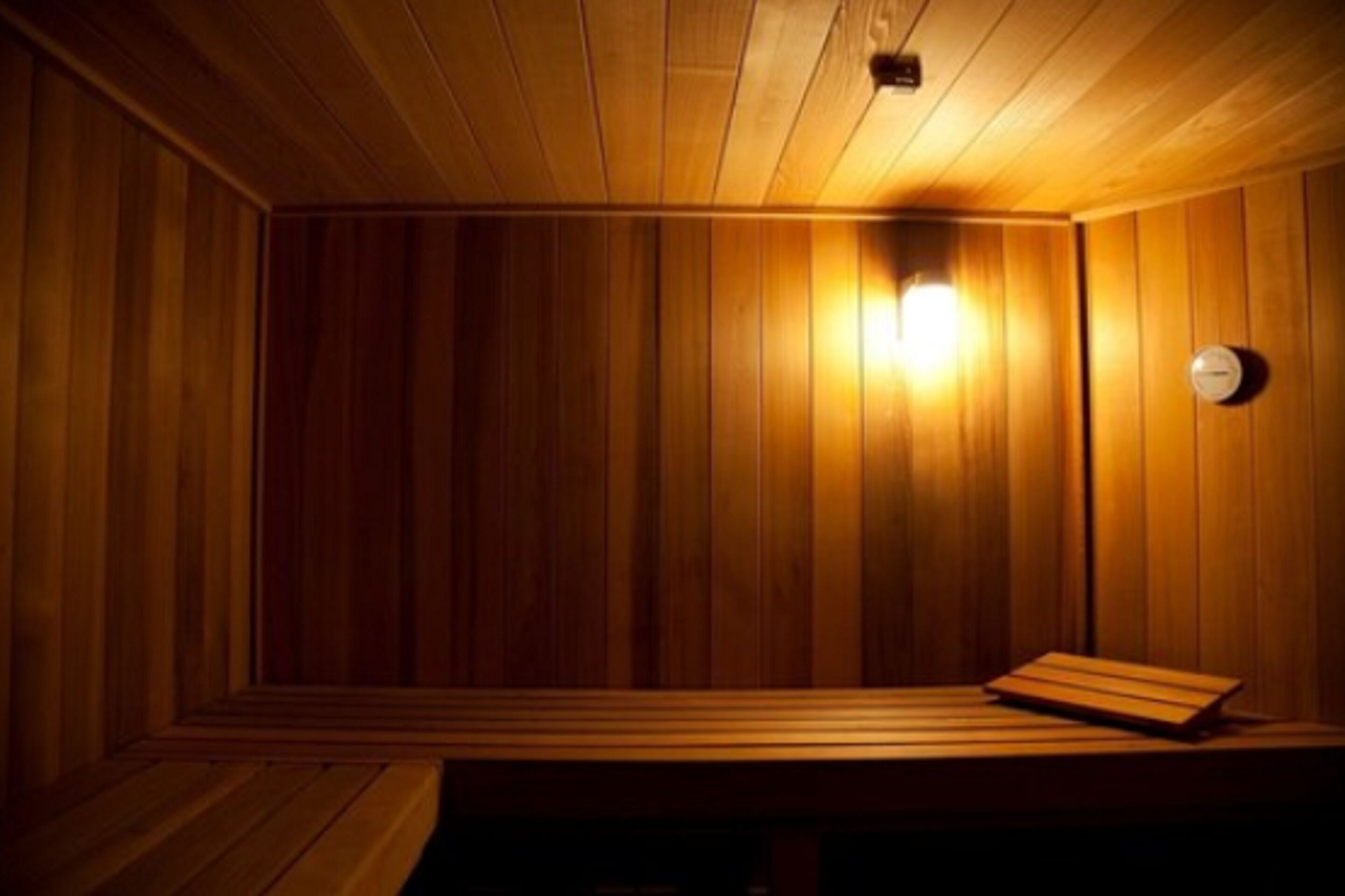 Una sauna de fusta amb una banca i una làmpada penjada a la paret.