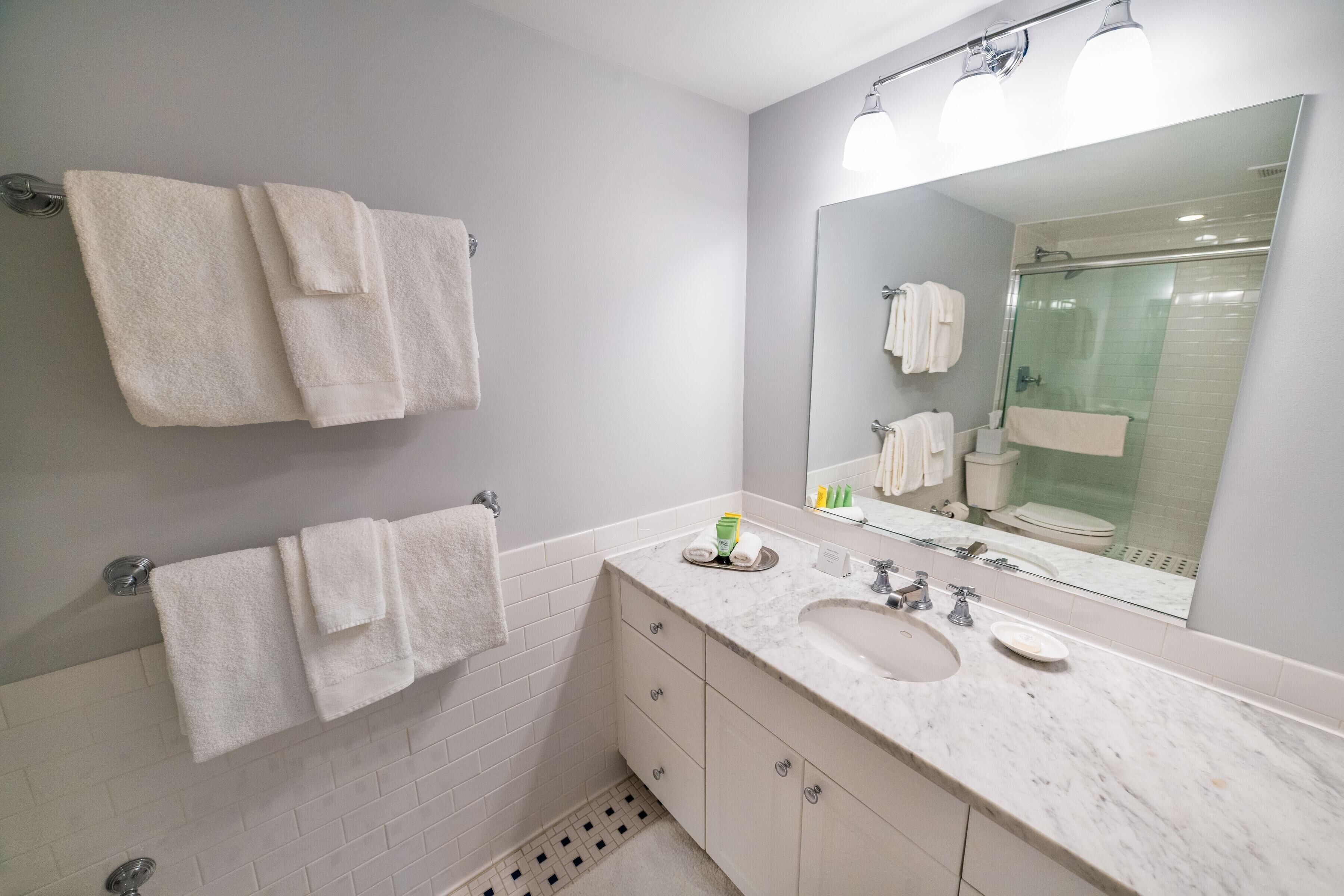 A modern bathroom with a large mirror, white tiles, a sink, and two towels hanging on the wall.