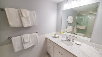 A modern bathroom with a large mirror, white tiles, a sink, and two towels hanging on the wall.