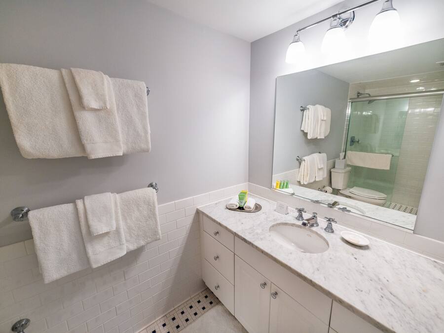 A modern bathroom with a large mirror, white tiles, a sink, and two towels hanging on the wall.