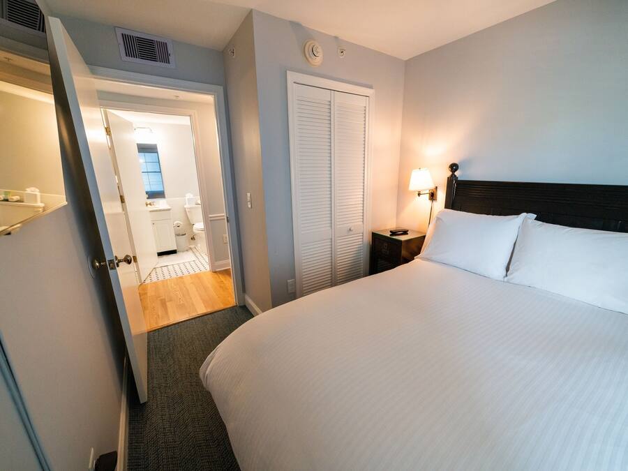 A hotel room with a large bed, a bedside table with a lamp, a wardrobe, and a bathroom visible through an open door.