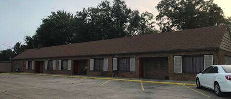 A single-story motel with a brick facade, multiple windows with shutters, and a parking lot with a white car parked in front.